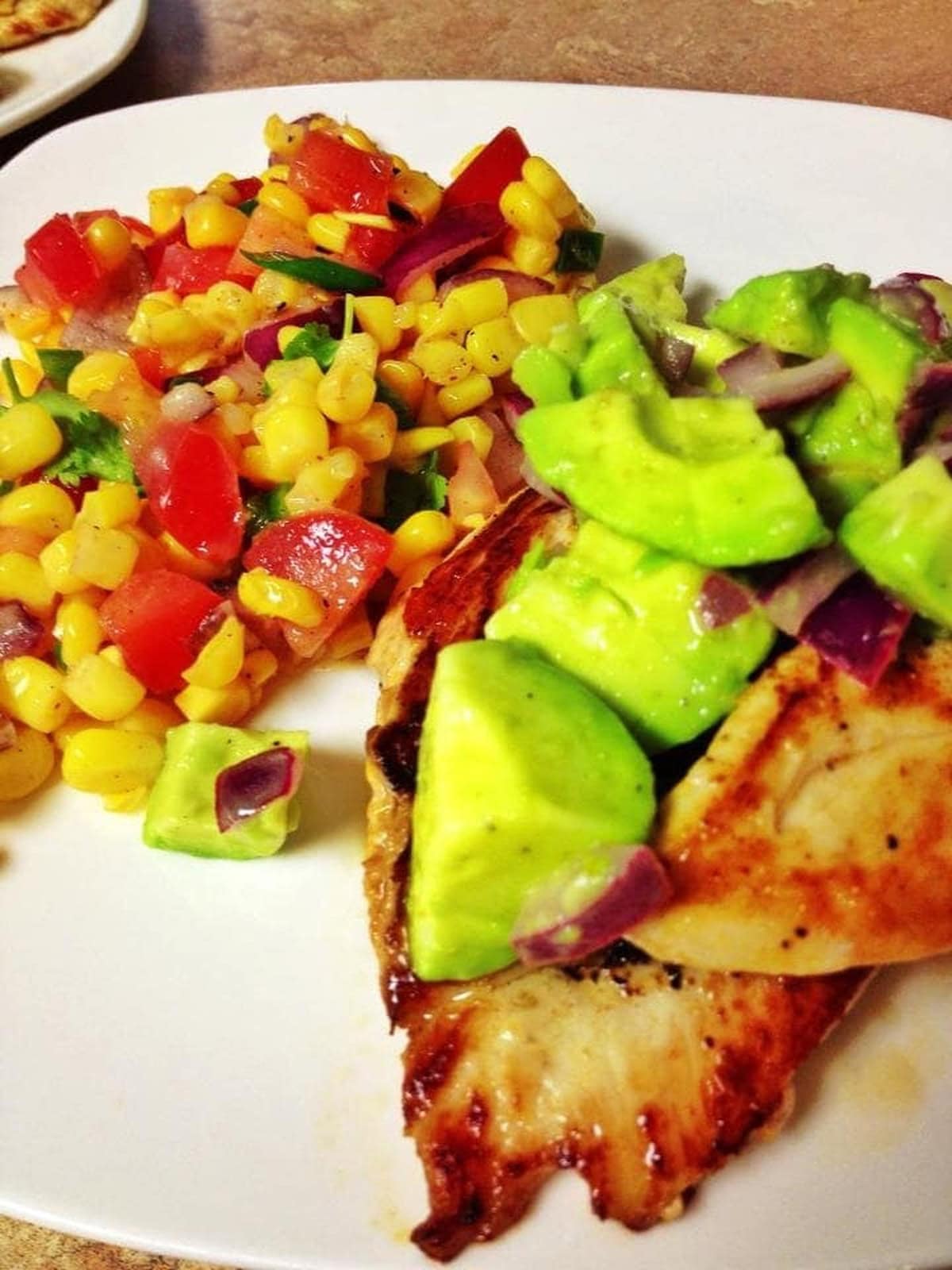 Finished avocado chicken and corn salsa on a plate.