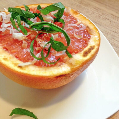 Broiled grapefruit half with toasted coconut flakes and sliced mint on a white plate.