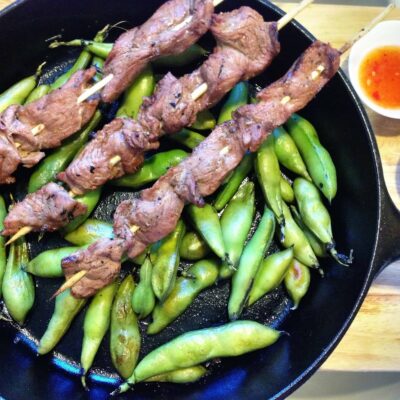 Grilled fava beans and beef kabobs cooking in a cast iron skillet.