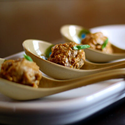 Three coconut curry meatballs served on tasting spoons.