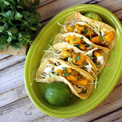 Baja fish tacos on a green plate with limes.