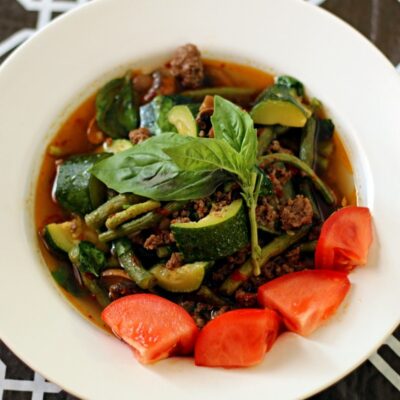 Thai beef soup garnished with tomato and basil leaves.