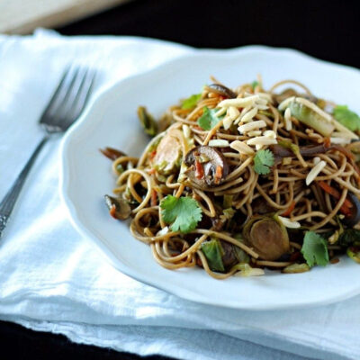 A plate of vegetable and noodle stir fry garnished with fresh cilantro and slivered almonds.