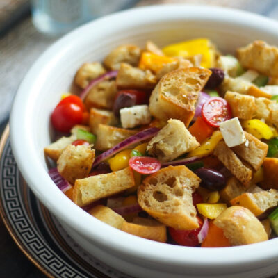 A white bowl of panzanella salad with toasted bread.