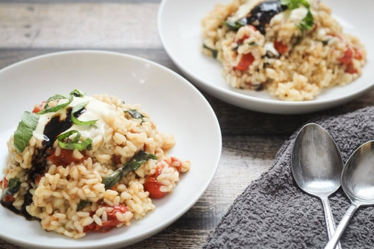 Burst tomato and basil risotto topped with mascarpone and balsamic glaze in a white bowl.