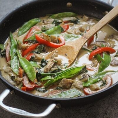 A pan with Thai green curry with a wooden spoon.