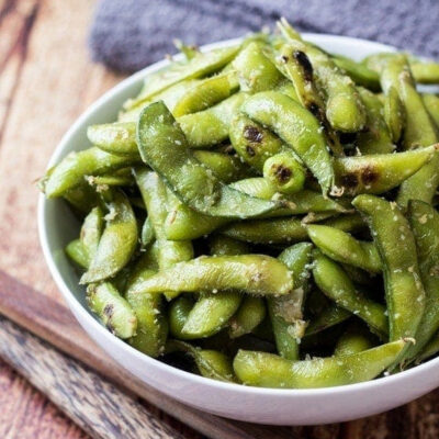 A bowl of garlic edamame on a wooden table.