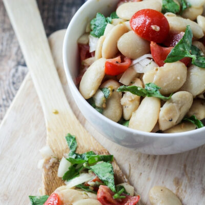 A close-up of Uruguayan Tomato White Bean Salad in a white bowl with a wooden spoon.