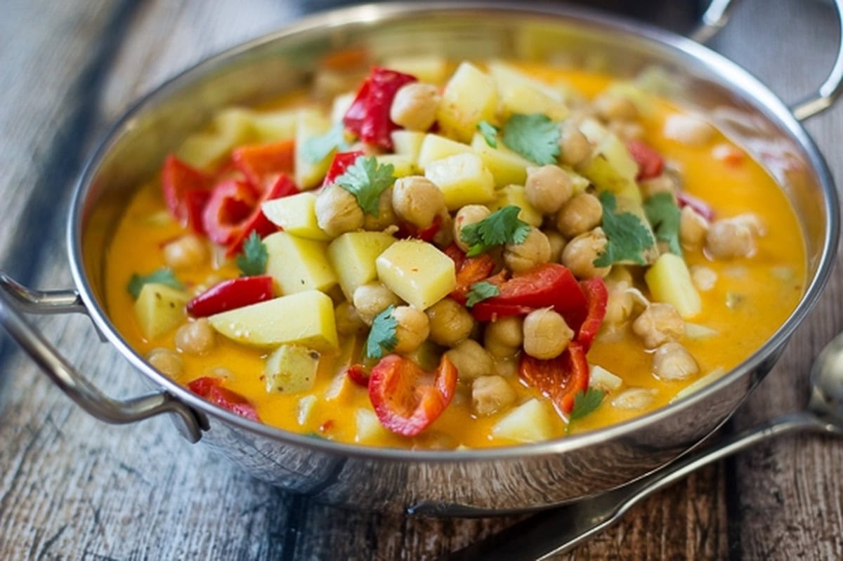 Chickpeas, potatoes, and red peppers simmered in curry sauce in a steel pan.