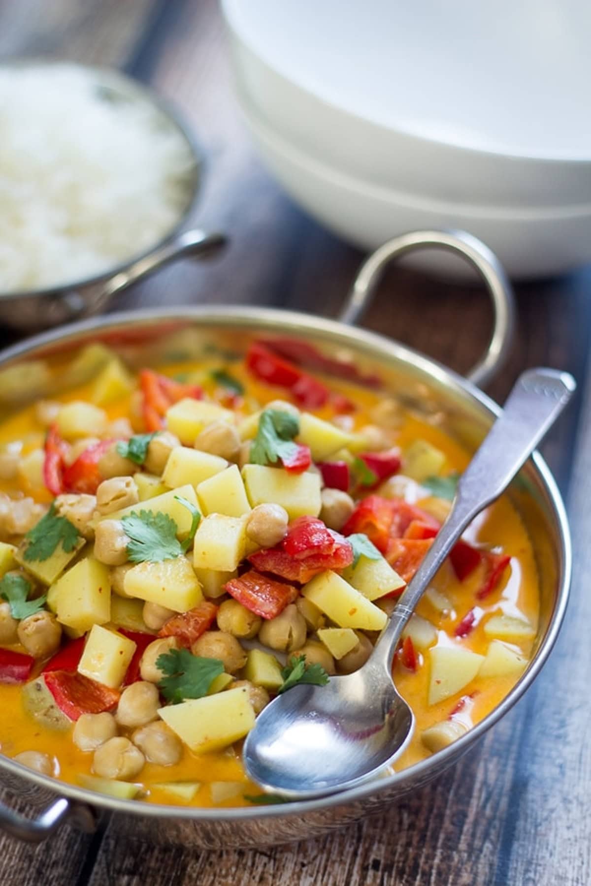 Spoon resting in easy chickpea curry with potatoes and red pepper in a steel dish.