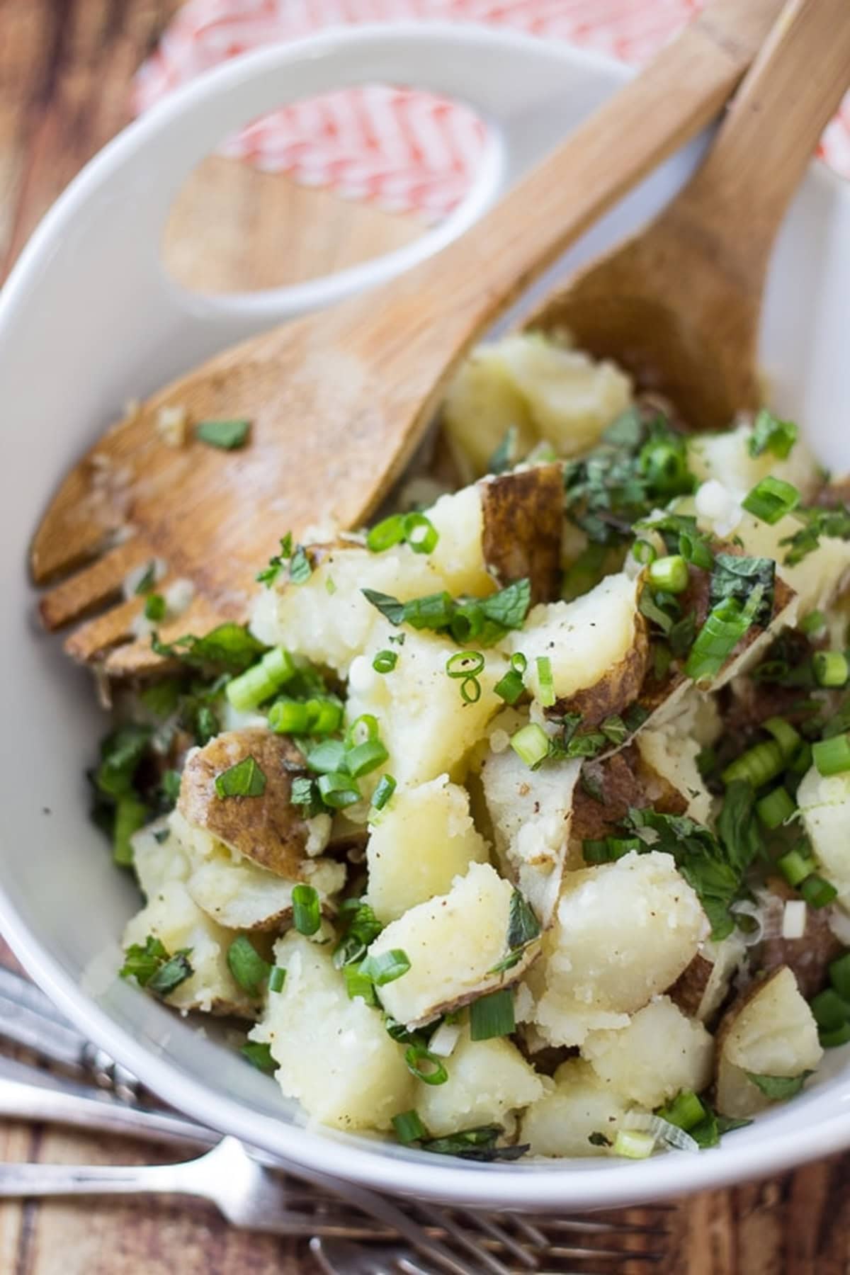 Lebanese potato salad served in a white bowl, with a wooden spoon resting inside.