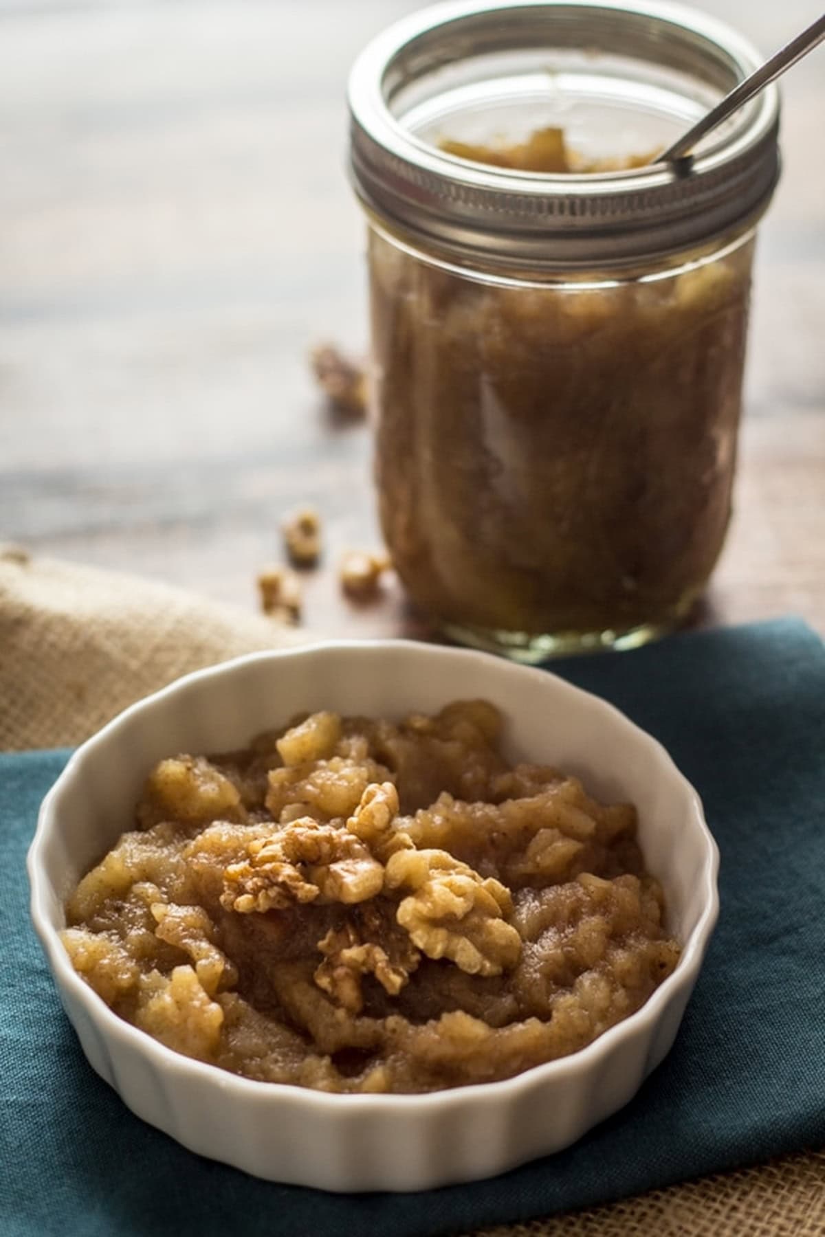 Warm crockpot applesauce in a bowl, topped with walnuts, with a jar behind it.