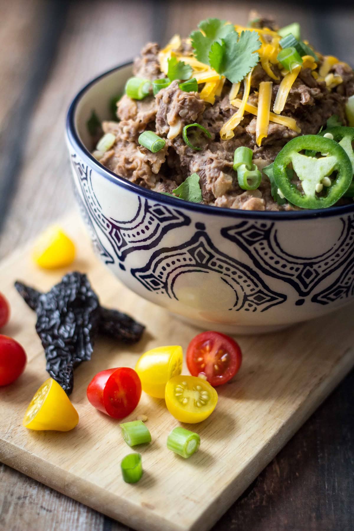 Refried beans served in a bowl, garnished with lime, cheese, and jalape&ntilde;os, with tomatoes and dried chilies on the side.