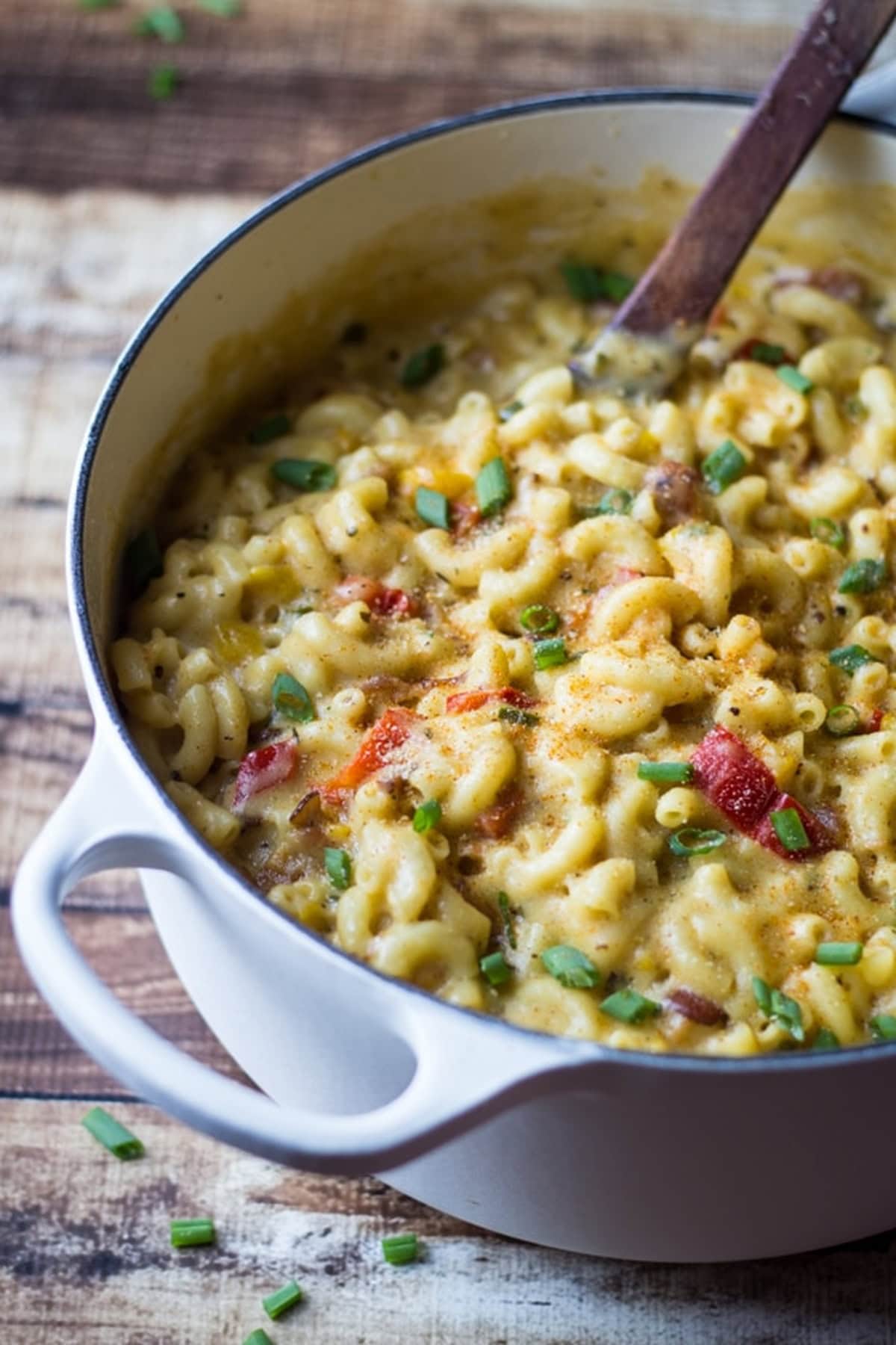 Creamy Cajun macaroni and cheese in a white pot with a wooden spoon.