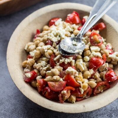 A bowl filled with chickpea salad with feta, garnished with herbs.