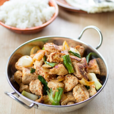 A bowl of rice and Malaysian Stir Fried chicken on a table.