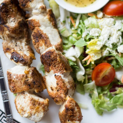 Mediterranean chicken kabobs, fresh salad, and a lemony dipping sauce on a plate.