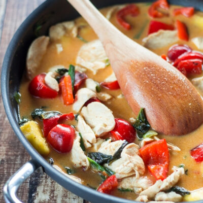 Thai red curry with chicken in a skillet with a wooden spoon resting on top.