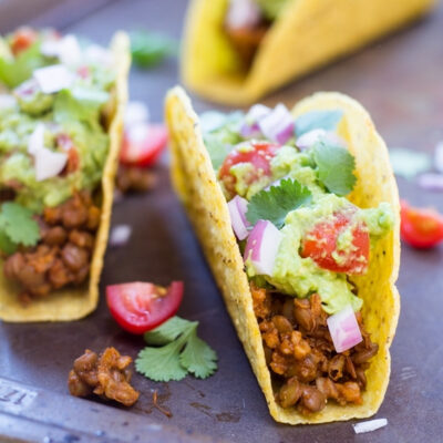 Close-up of a Vegan Lentil Taco topped with guacamole, diced red onion, and cilantro.