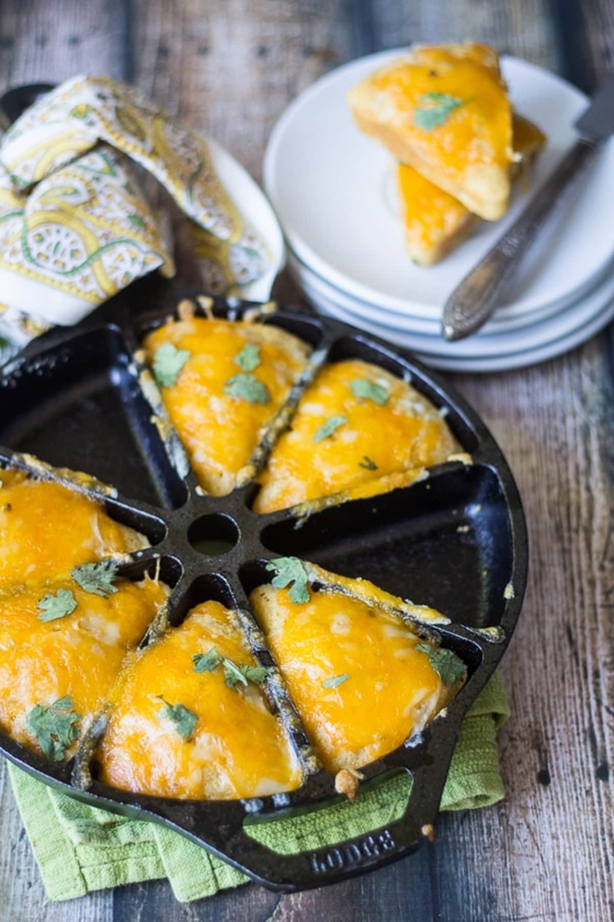 Cheesy Mexican cornbread wedges topped with melted cheddar and fresh cilantro in a cast iron skillet.