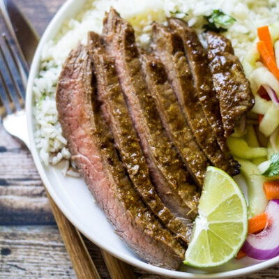Sliced Asian Flank Steak served over fluffy rice, garnished with a lime wedge.