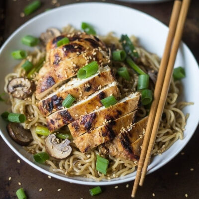 A bowl filled with noodles and topped with grilled Garlic ginger Chicken.