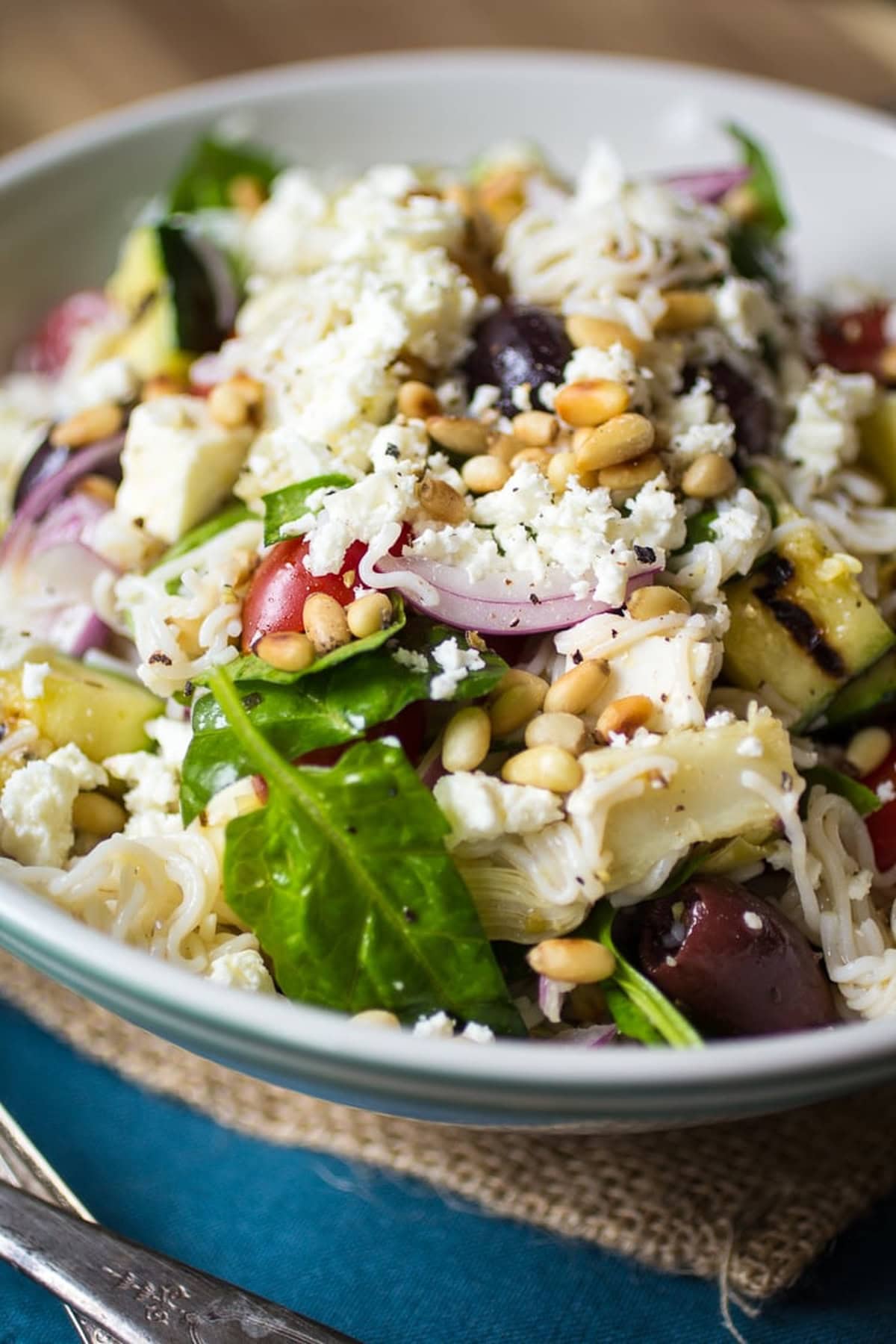 Mediterranean pasta salad topped with pine nuts and feta cheese in a bowl.