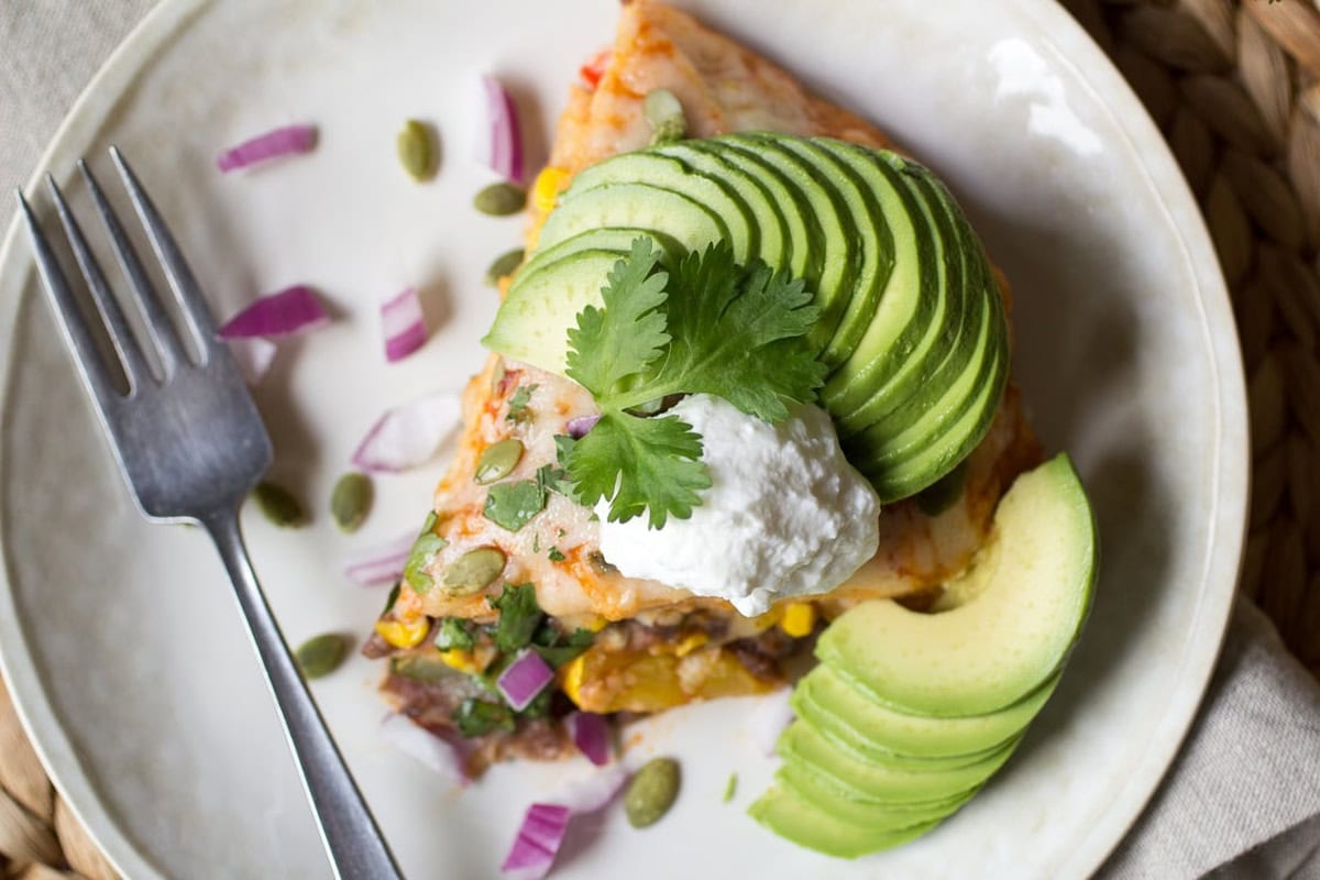 A side view of an enchilada pie slice on a white plate.