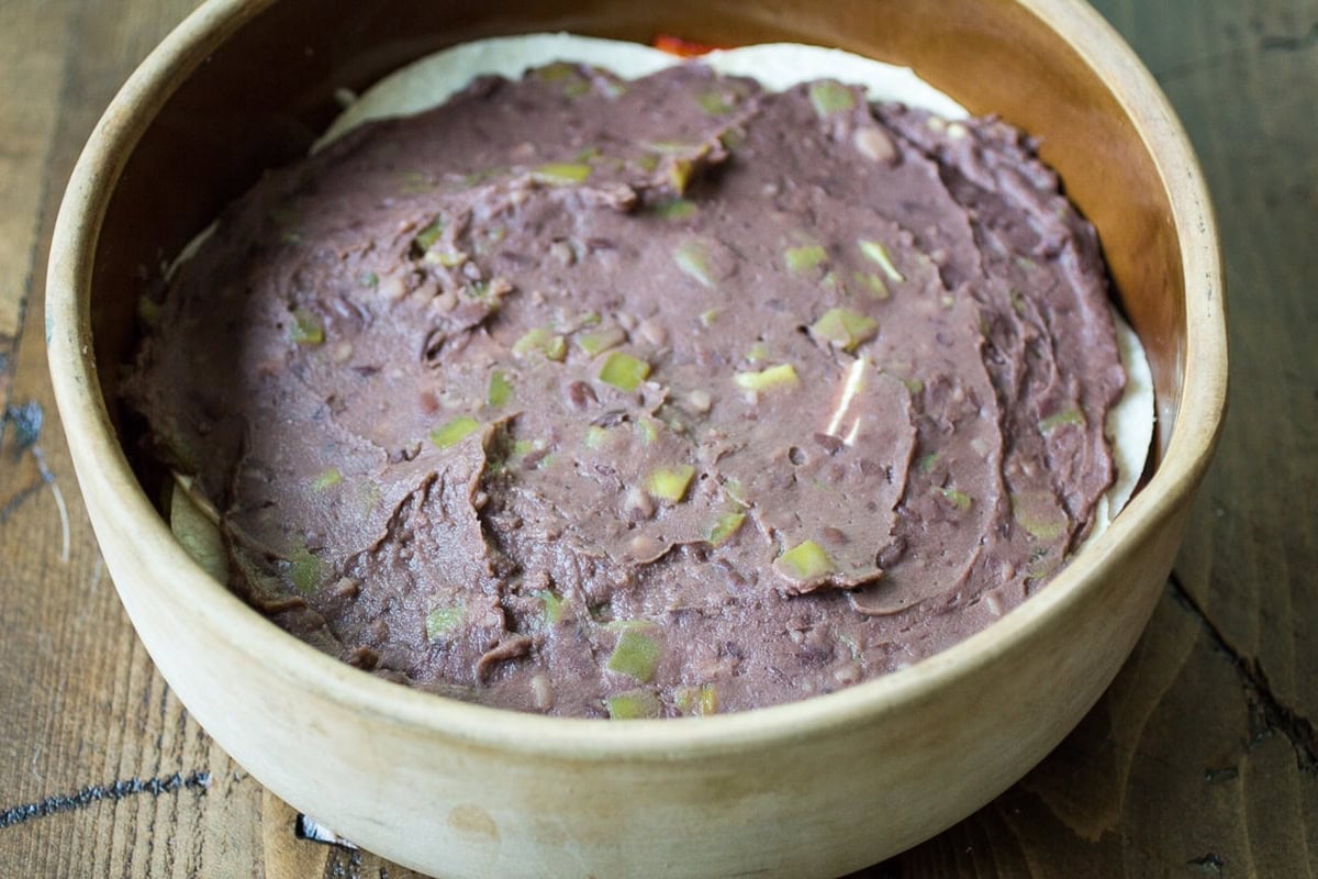 A wooden dish with a base layer of refried beans spread evenly.