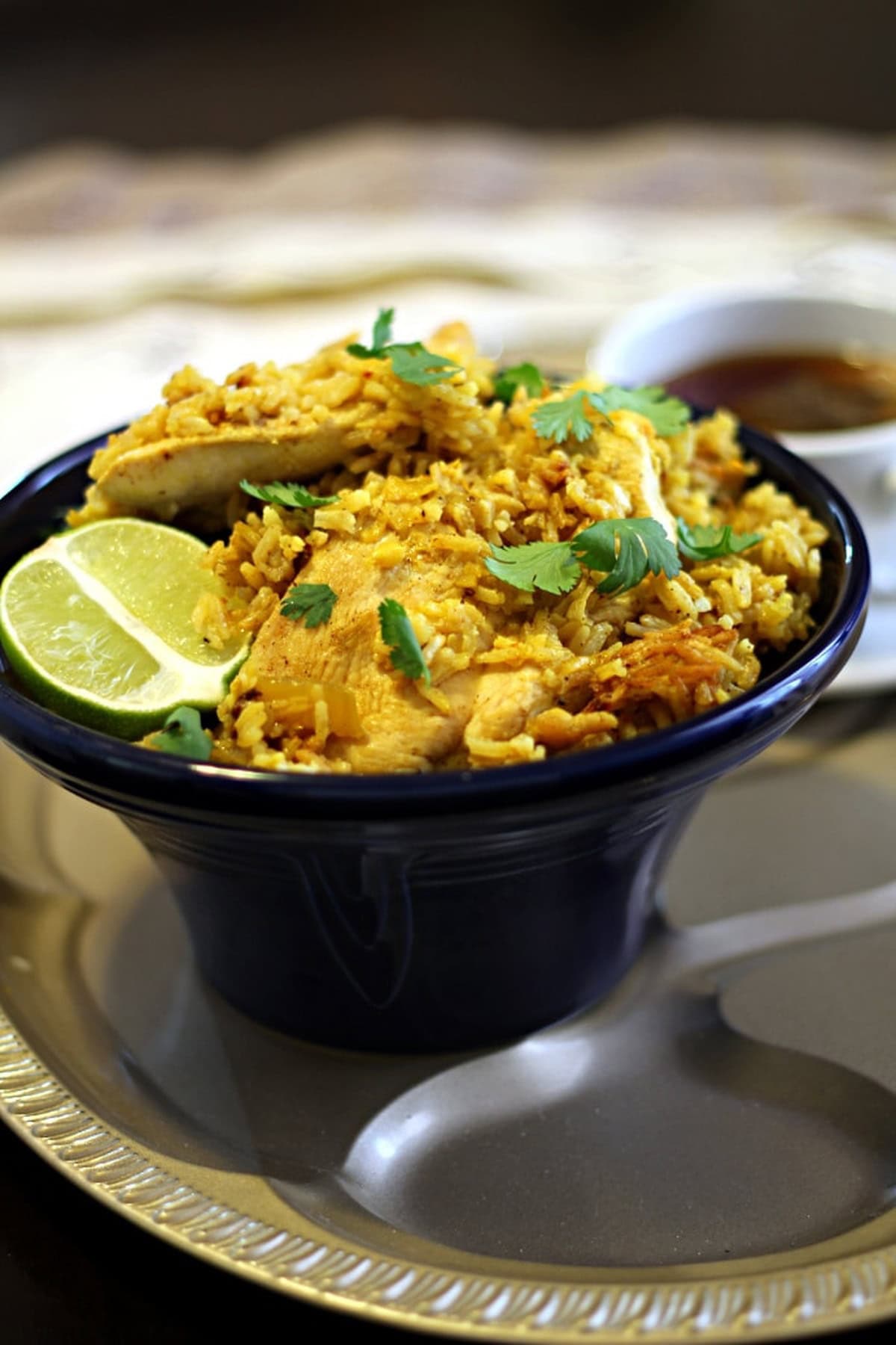 A bowl of Thai garlic chicken and rice garnished with cilantro and lime wedges.