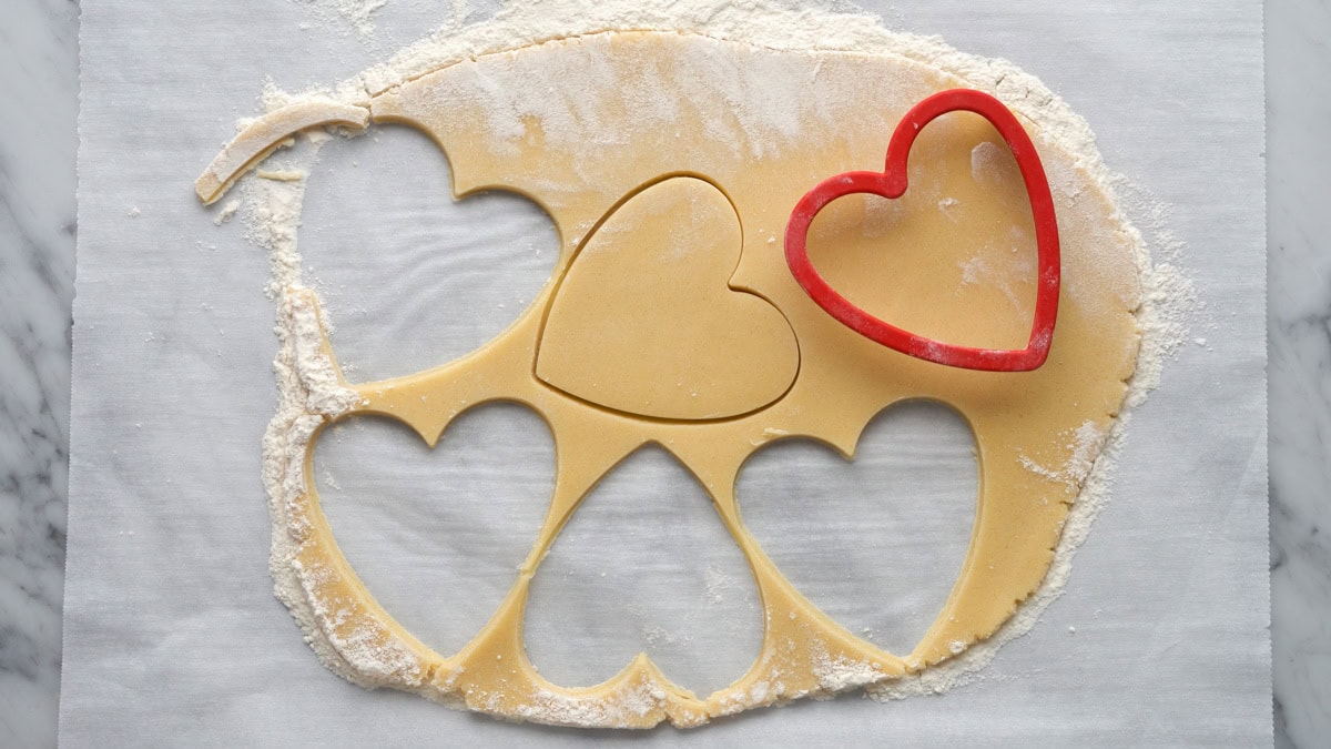 Hearts being cut out of rolled out cookie dough.