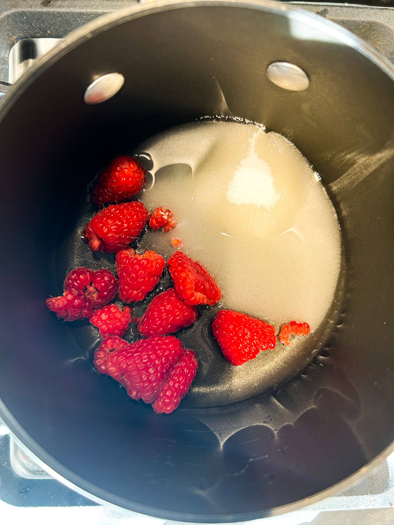 A pot with fresh raspberries, sugar, and water.