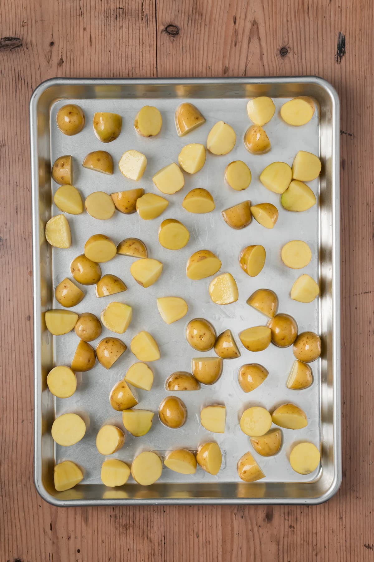 Potatoes coated in olive oil on a baking sheet.