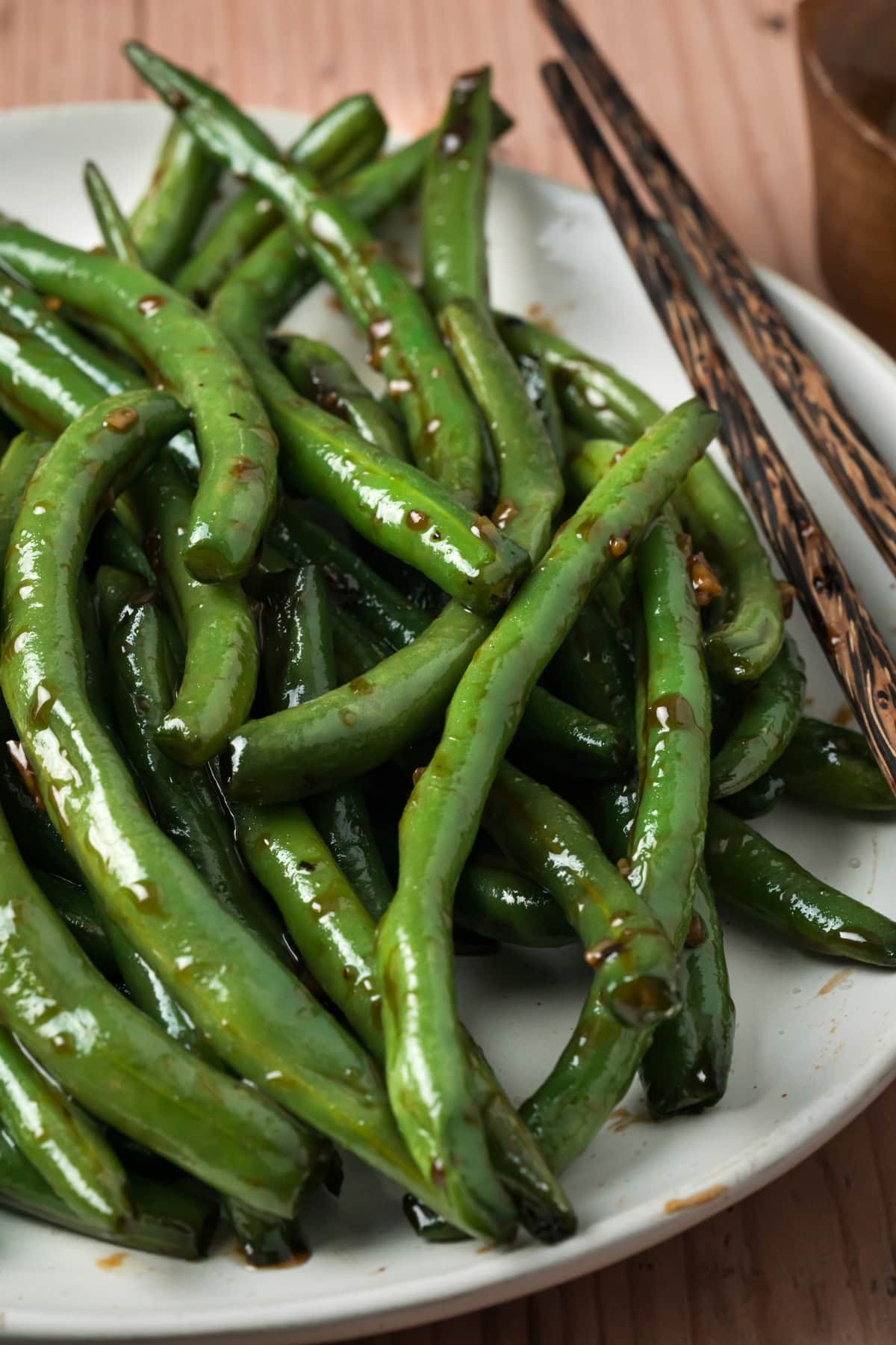 Chinese green beans on a white plate with chopsticks on the side.