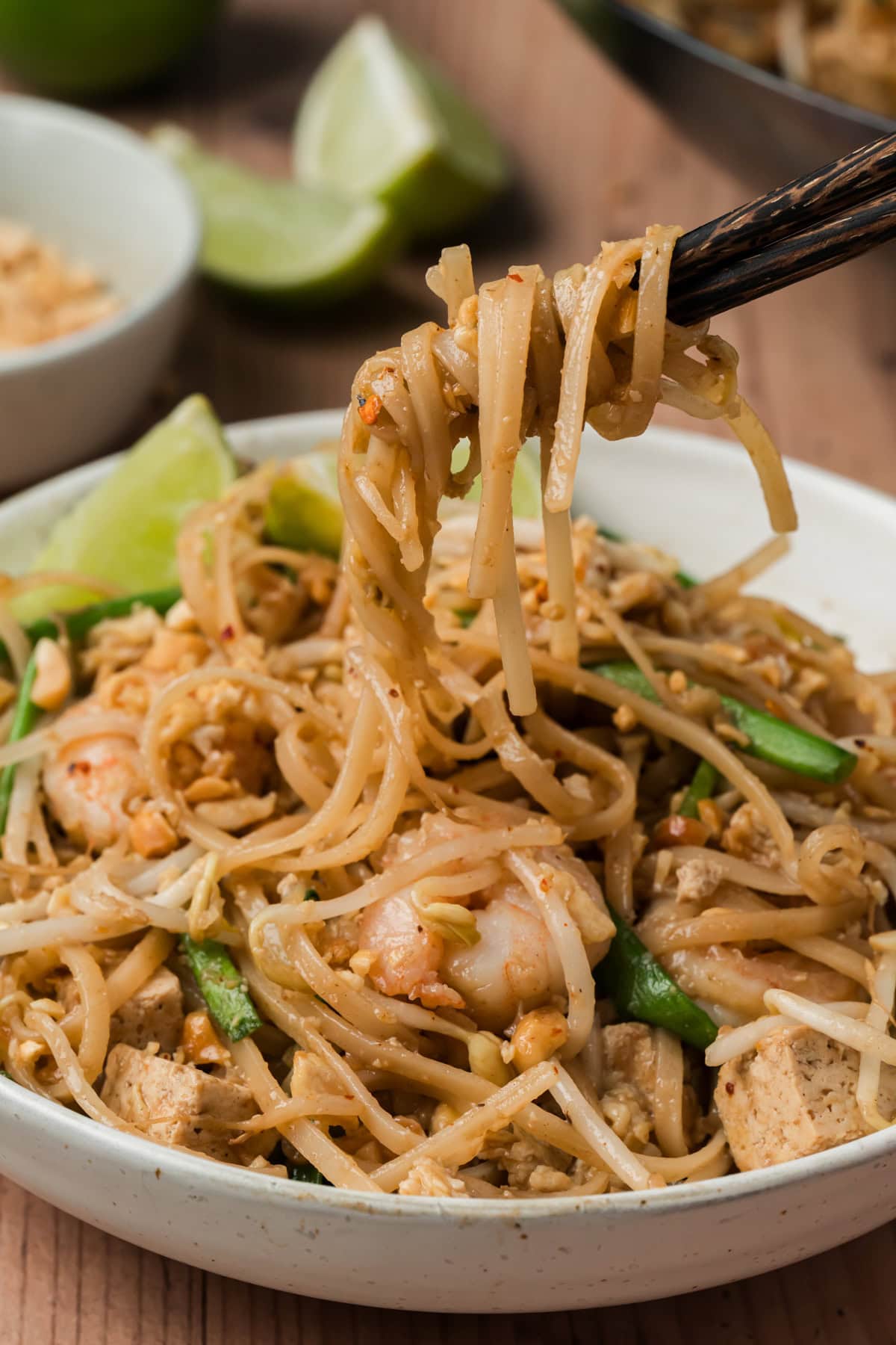 Chopsticks grabbing a bite of pad Thai from a bowl.