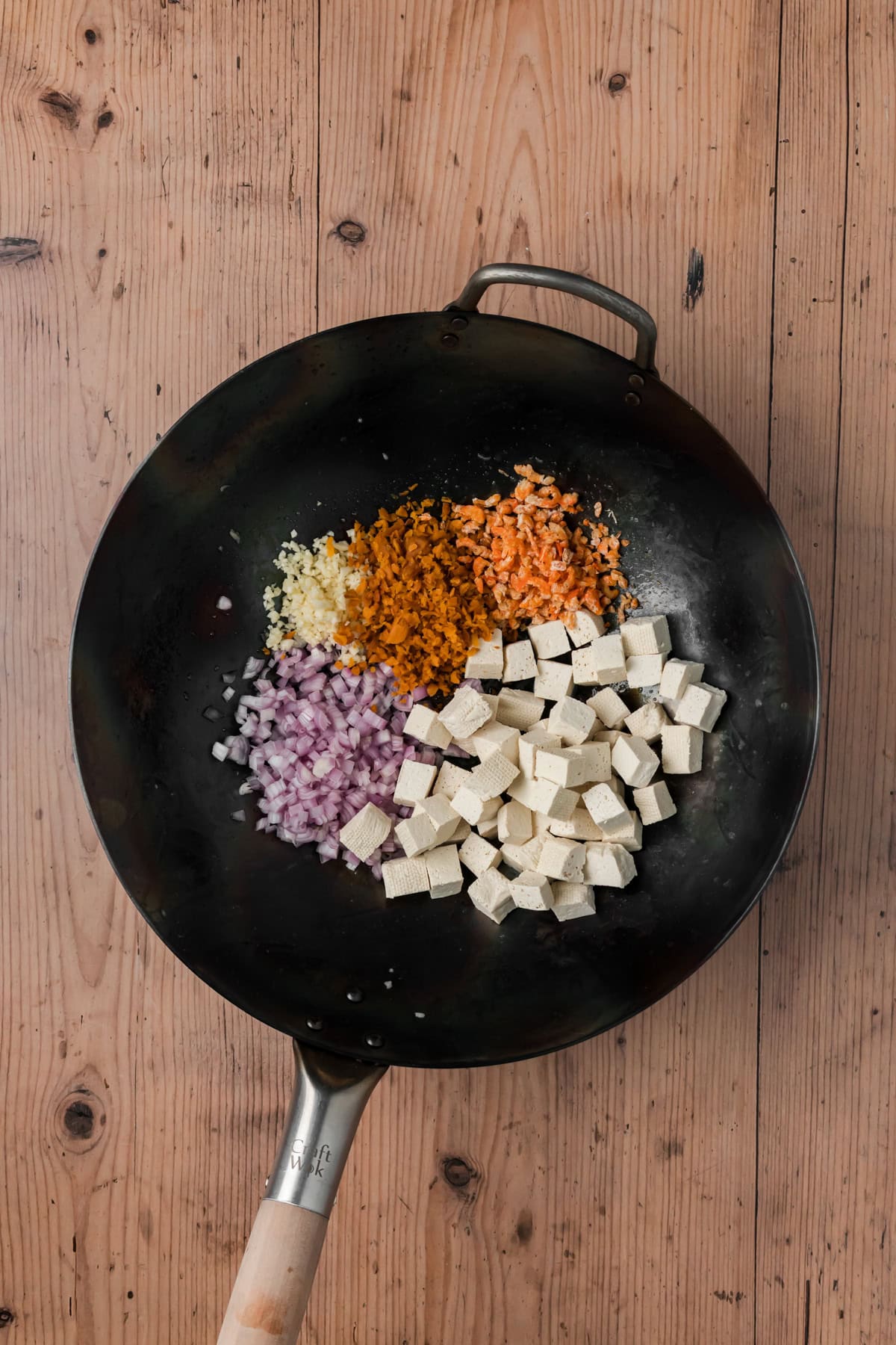 Garlic, shallots, tofu, preserved radish, and dried shrimp cooking in a wok.