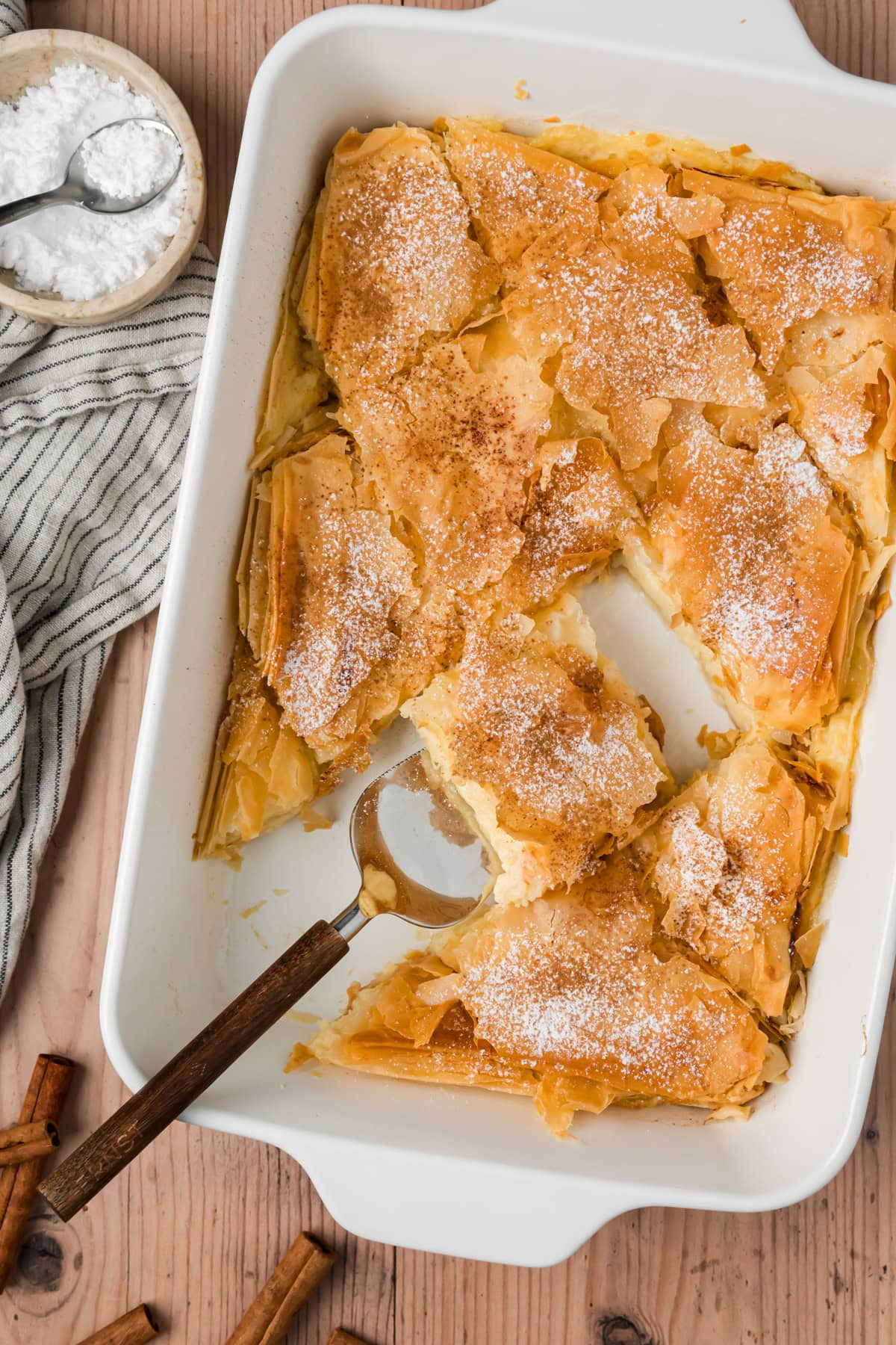 Bougatsa dusted with powdered sugar and cinnamon in a baking dish.