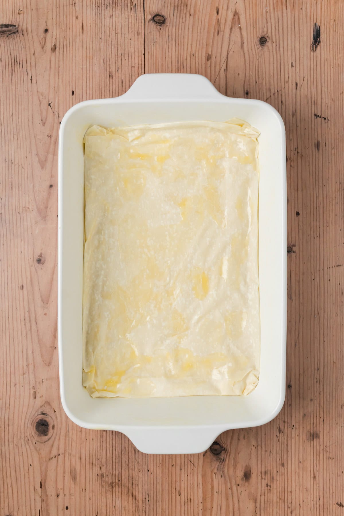 Phyllo sheets topped with butter and layered at the bottom of a baking dish.