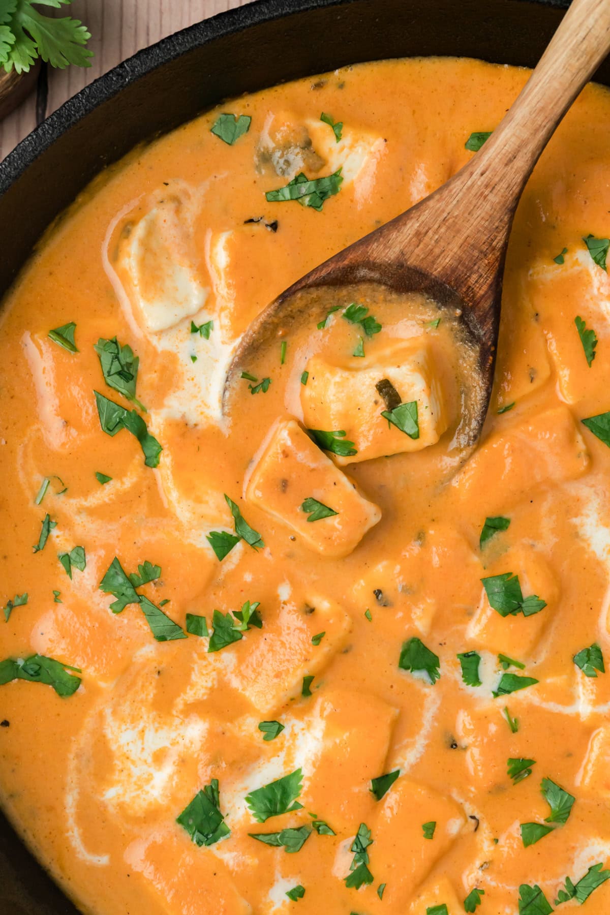 Paneer butter masala with a wooden spoon scooping some. 